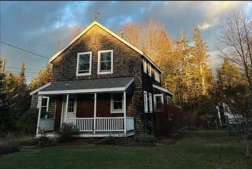 Shingled two-story house with a porch in autumn light