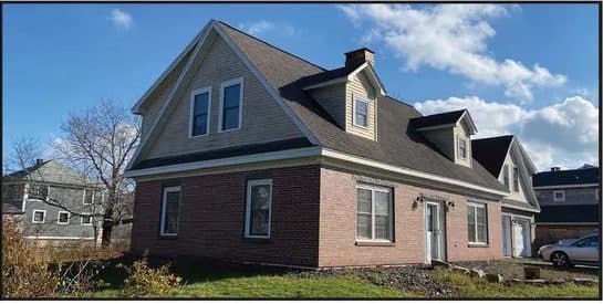 Brick and shingle house with dormers under a blue sky