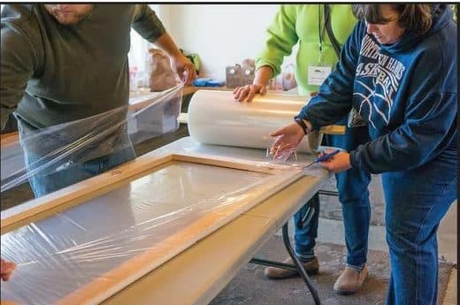 Volunteers stretching film over a wooden window insert frame